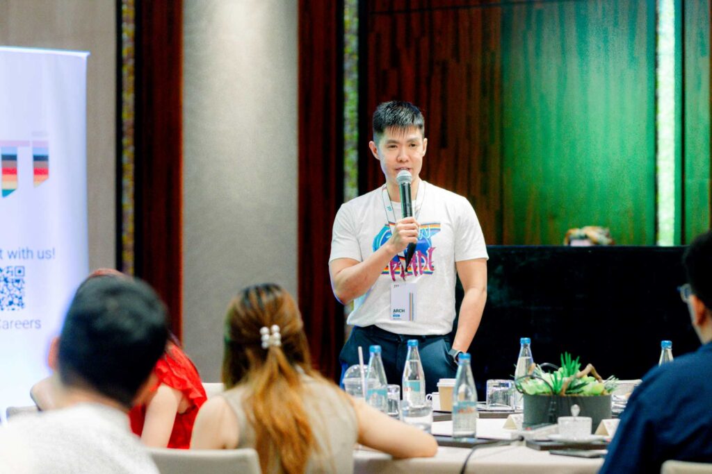 A man in a white T-shirt talking into a mic