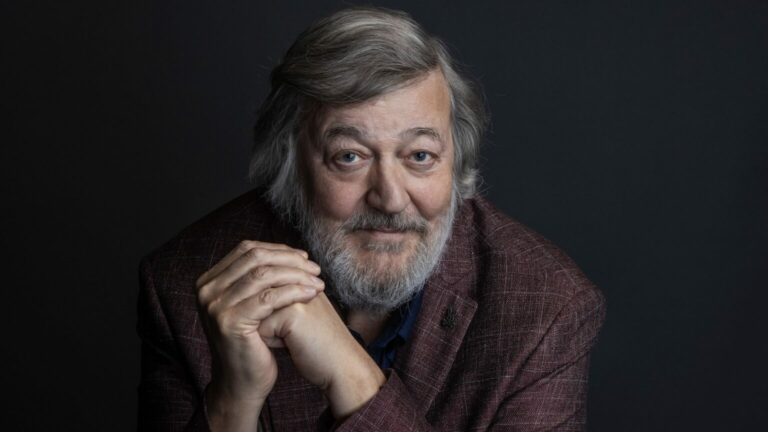 A portrait of Stephen Fry wearing a brown jacket