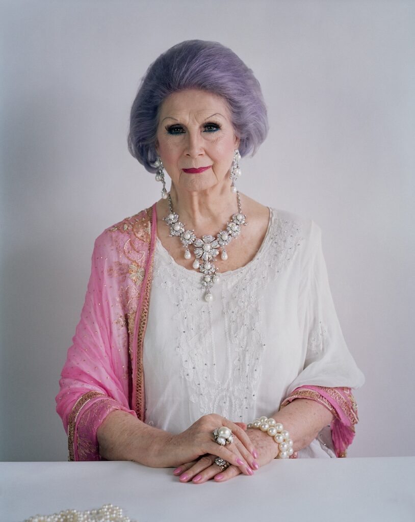 April Ashley with purple hair, wearing jewellery and a white gown