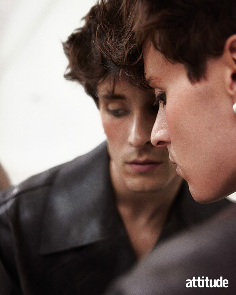 Calvin leans against mirror in oversized leather trench