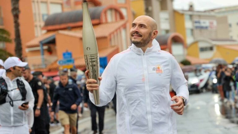 A man in a white poncho holding an Olympic Torch