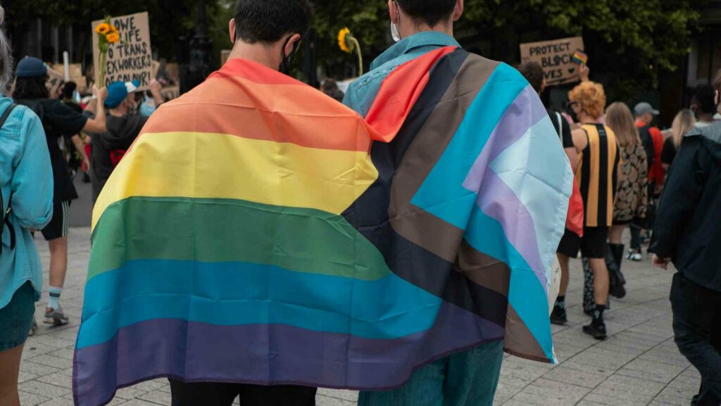 Two people wearing Pride flags in a crowd