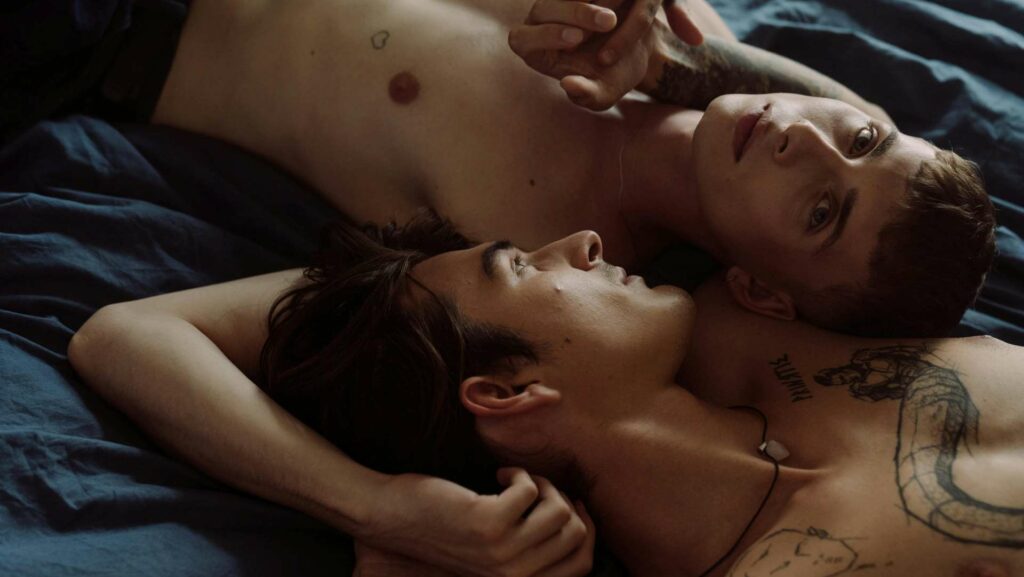 Two shirtless men lying on a bed