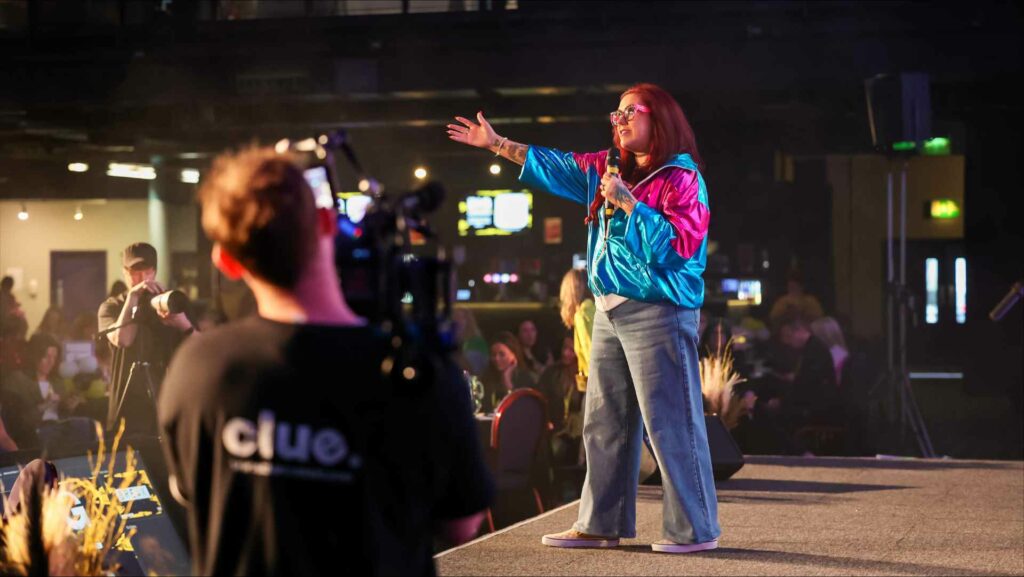 A woman stands on stage with a mic in her hand addressing an audience