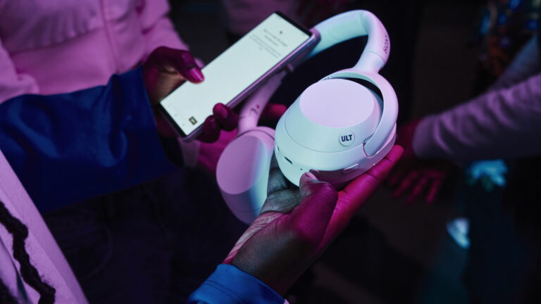 Close up of someone holding white Sony headphones and a smartphone