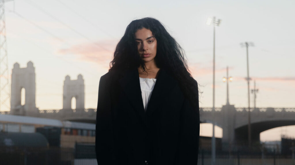 Charli xcx standing in front of a cityscape background.