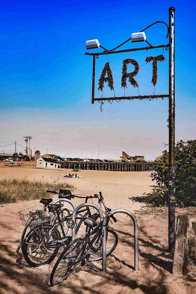 A rusted sign saying "art" standing in front of a beach in Provincetown