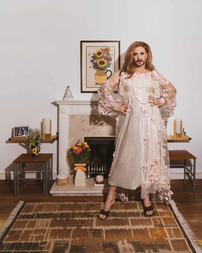 Jonny Woo in a floral dress standing in front of a fireplace