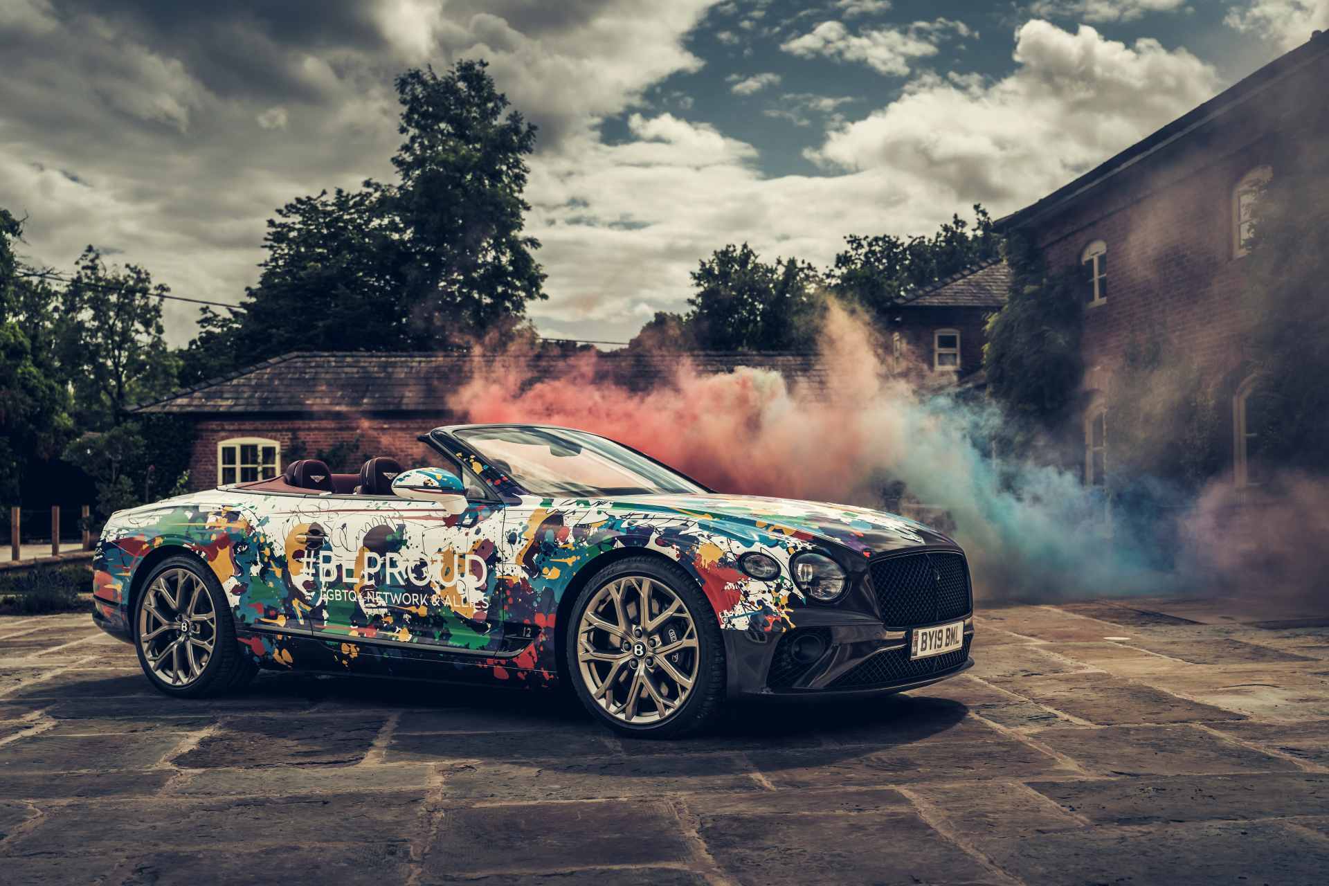 A rainbow coloured Bentley Continental GTC surrounded by rainbow coloured smoke