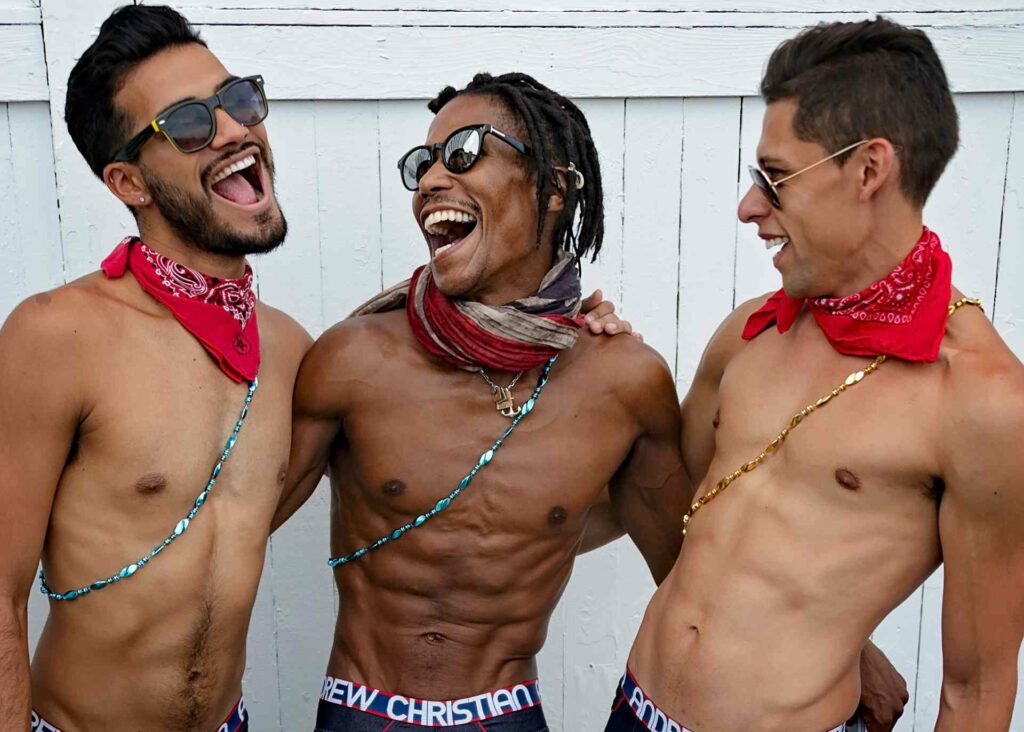 Three shirtless men embracing and laughing