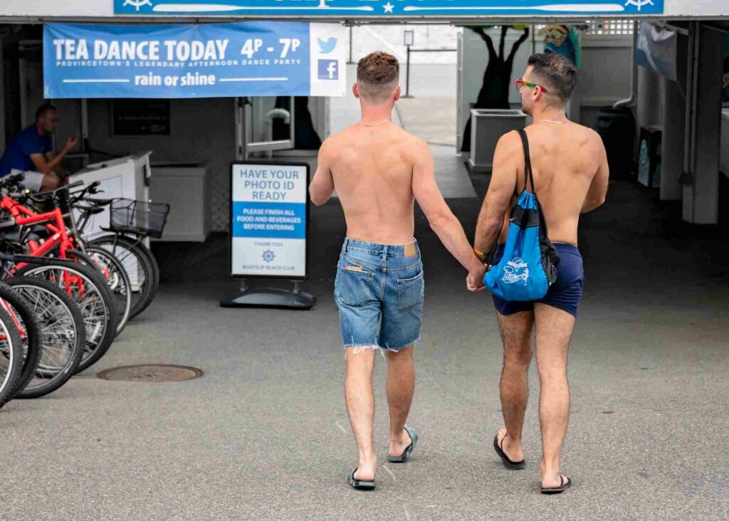 Two shirtless men holding hands as they enter the Tea Dance event in Provincetown