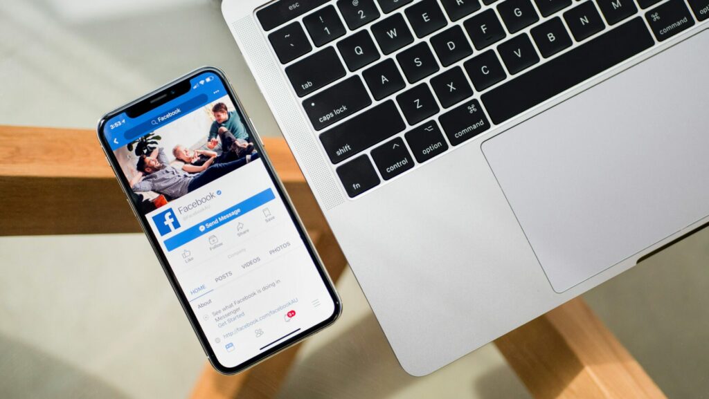 A phone displaying the Facebook app next to a laptop.