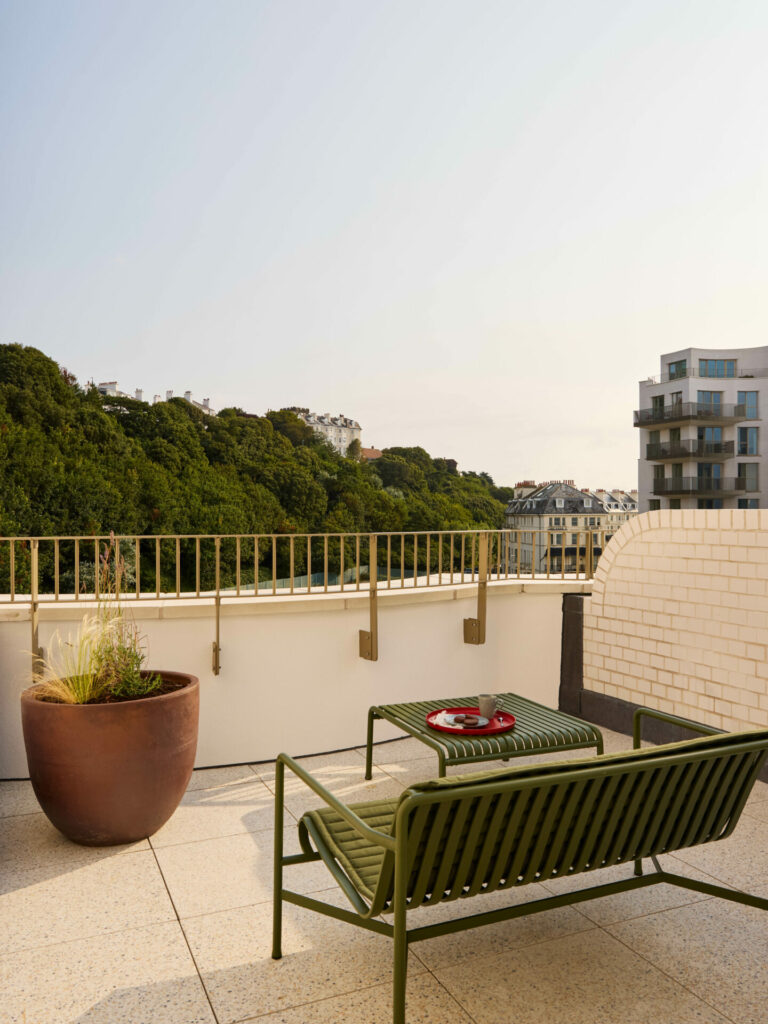 View of an outdoor terrace with a green bench and table overlooking trees