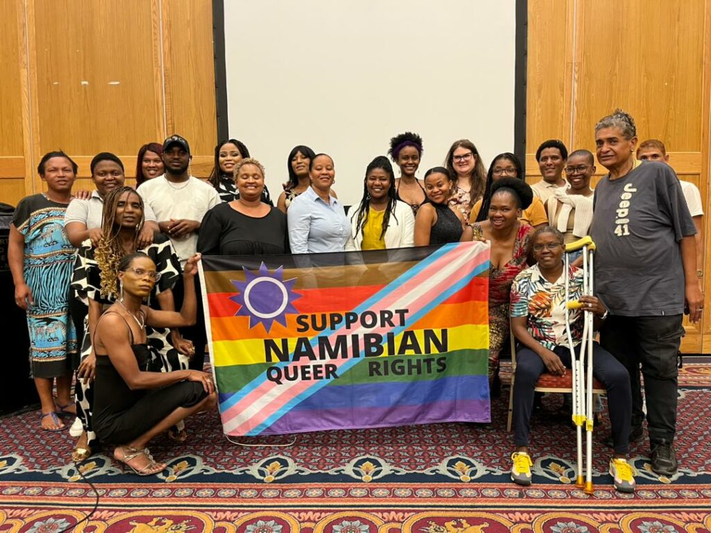 A group of people posing around a flag saying support Namibian queer rights on it