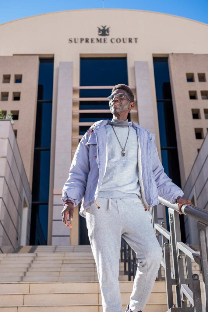 A man wearing a grey tracksuit and purple jacket standing on steps outside a Supereme Court