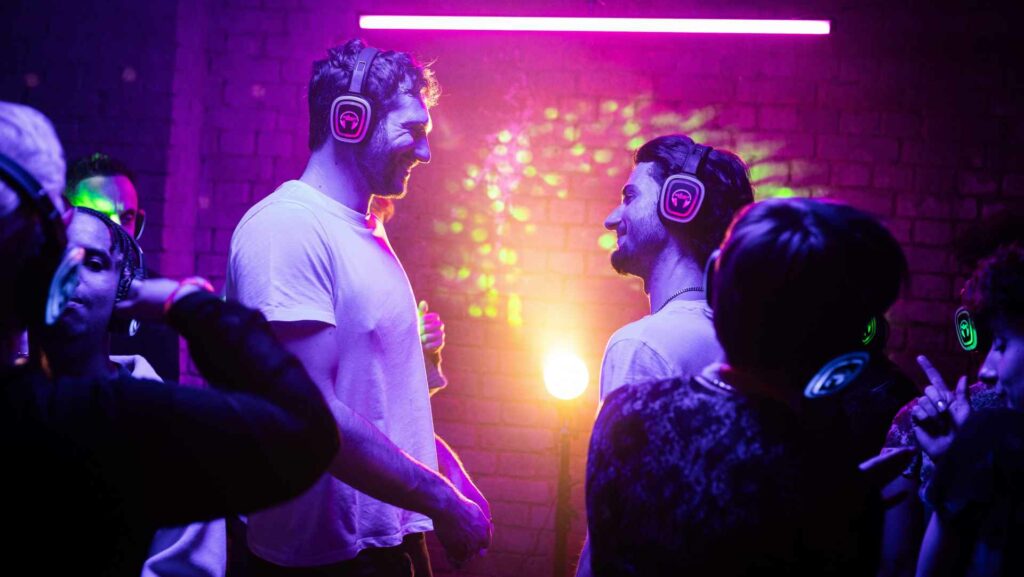 A still from A Night Like This, two mean in headphones staring at each other