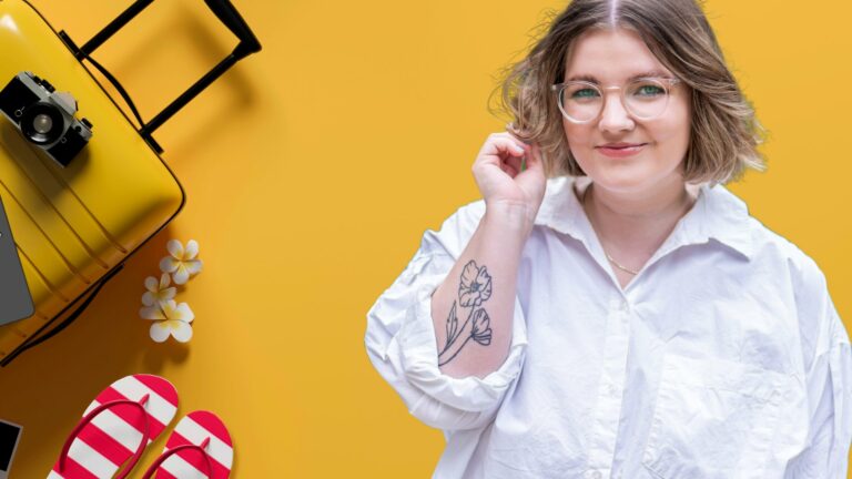 A smiling woman wearing glasses and a white blouse against a yellow backdrop with a suitcase and camera