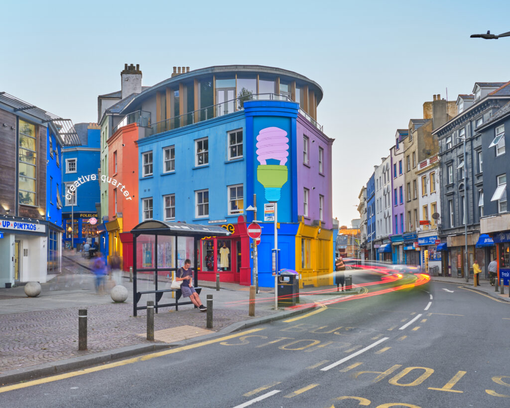 Folkestone's Old High Street, showing a colourful building with a bus stop outside it with a person sitting at it