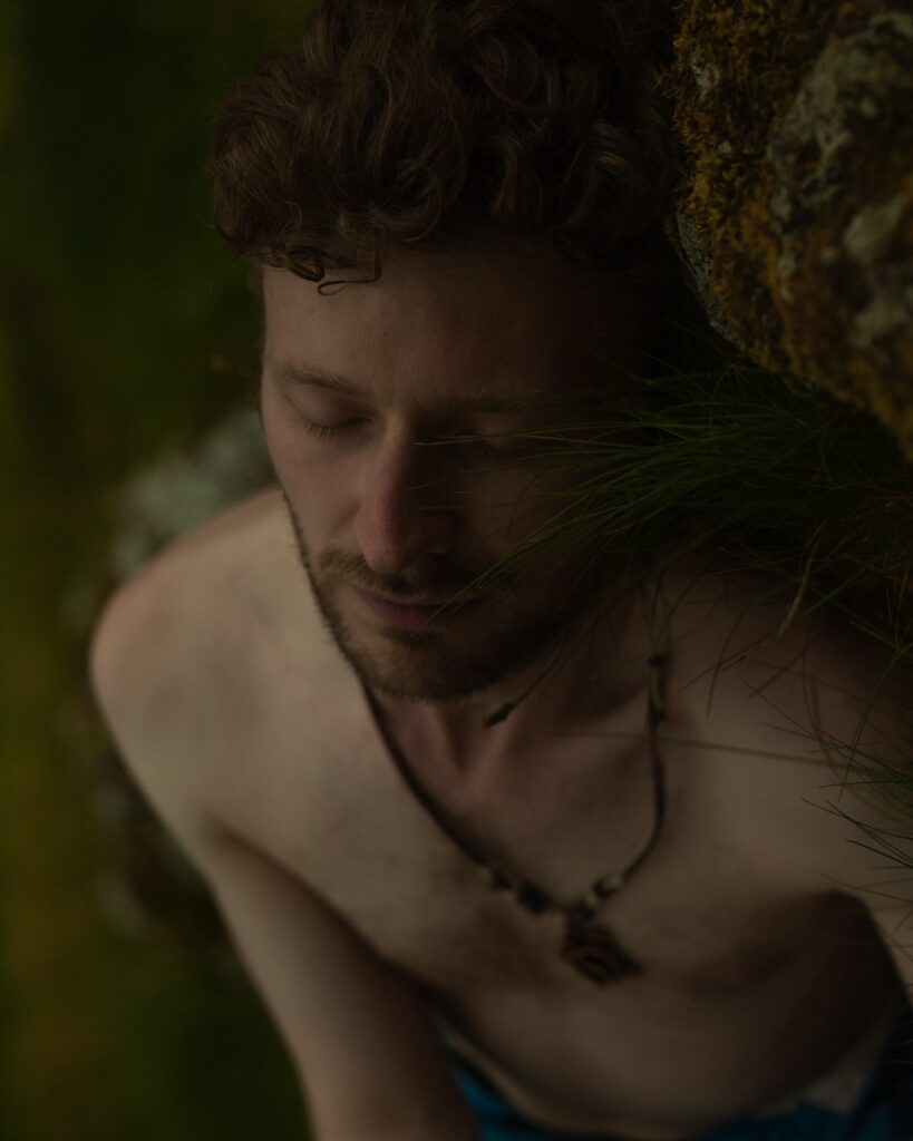 a topless man lying down next to some moss