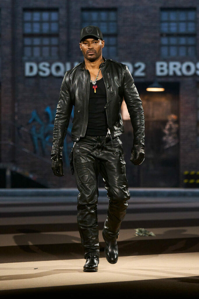 Tyson Beckford walks the runway in a head-to-toe leather look, featuring a sleek jacket, gloves, trousers road-ready trucker hat.