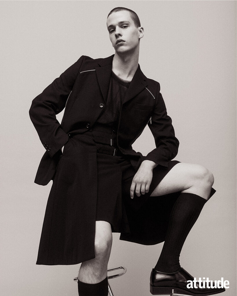 Model poses in black over coat with short black shorts, long black socks & formal shoes