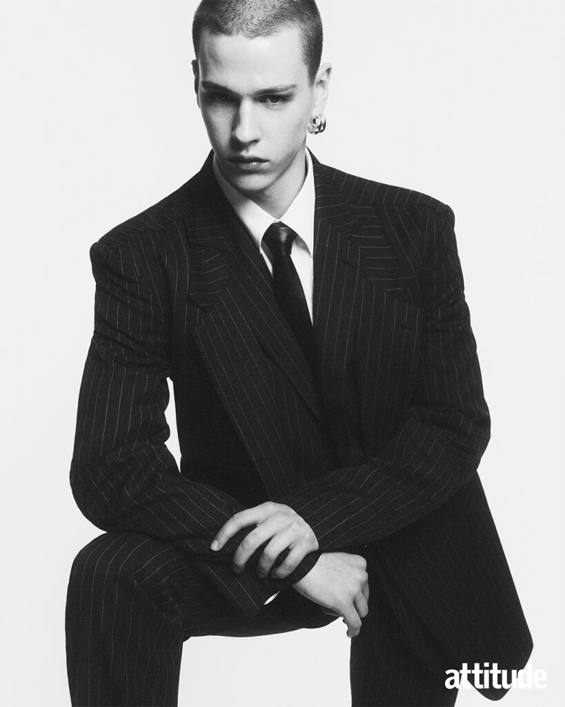 Model poses in pinstripe black suit with white shirt, black tie and chunky silver hoop earring