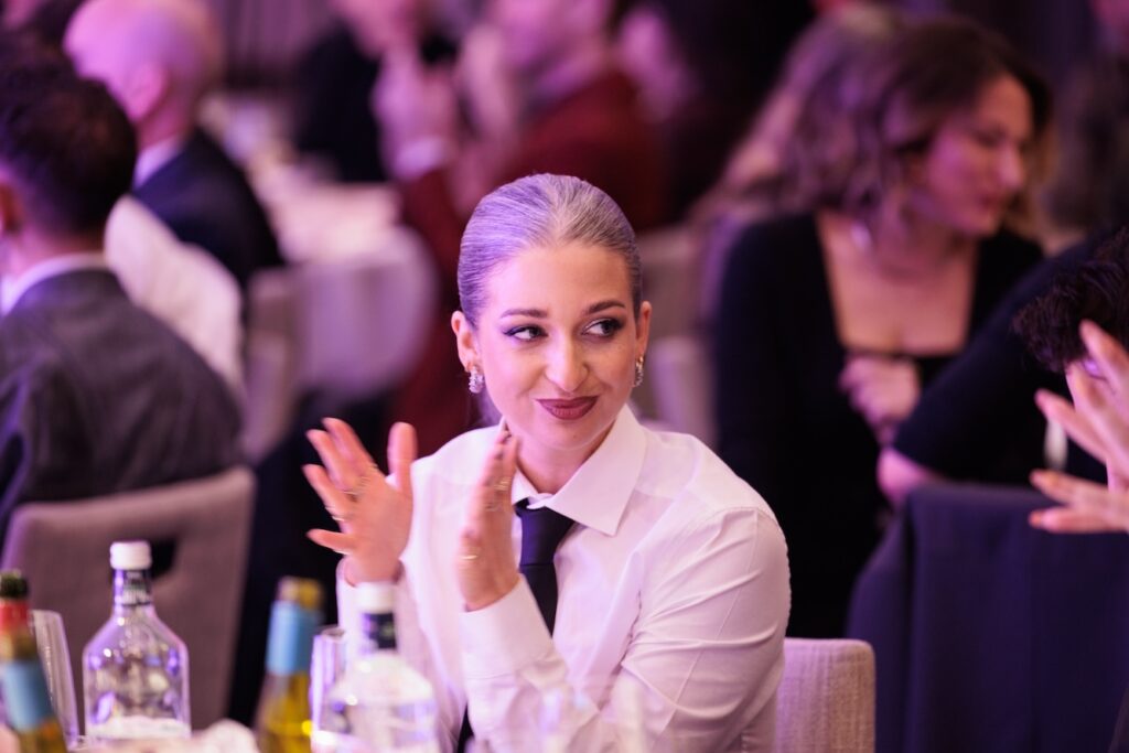 Harriet Rose in a white shirt and black tie, sat at lunch