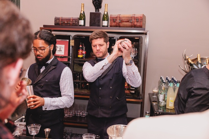 two mixologists at a bar shaking cocktail makers 