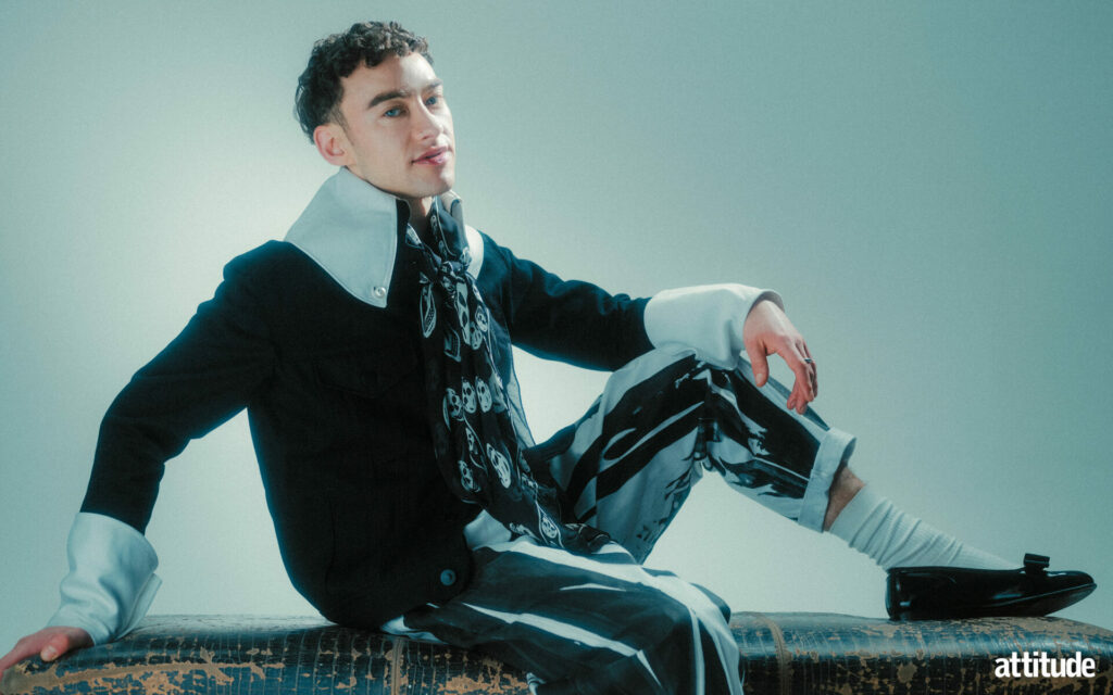 Olly Alexander in a shoot from his new Attitude cover shoot, sitting down in a collared shirt and matching trousers