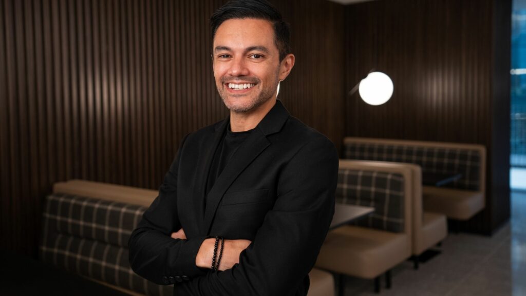 A smiling man wearing a black suit with his arms crossed