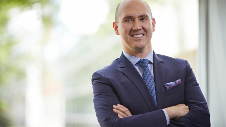 A smiling man in a blue business suit with his arms folder