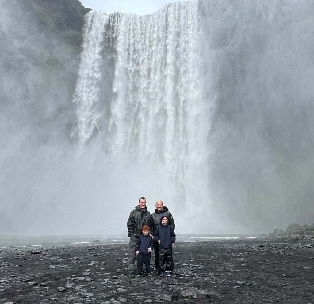 Two fathers and their two children standing in front of a tall waterfall