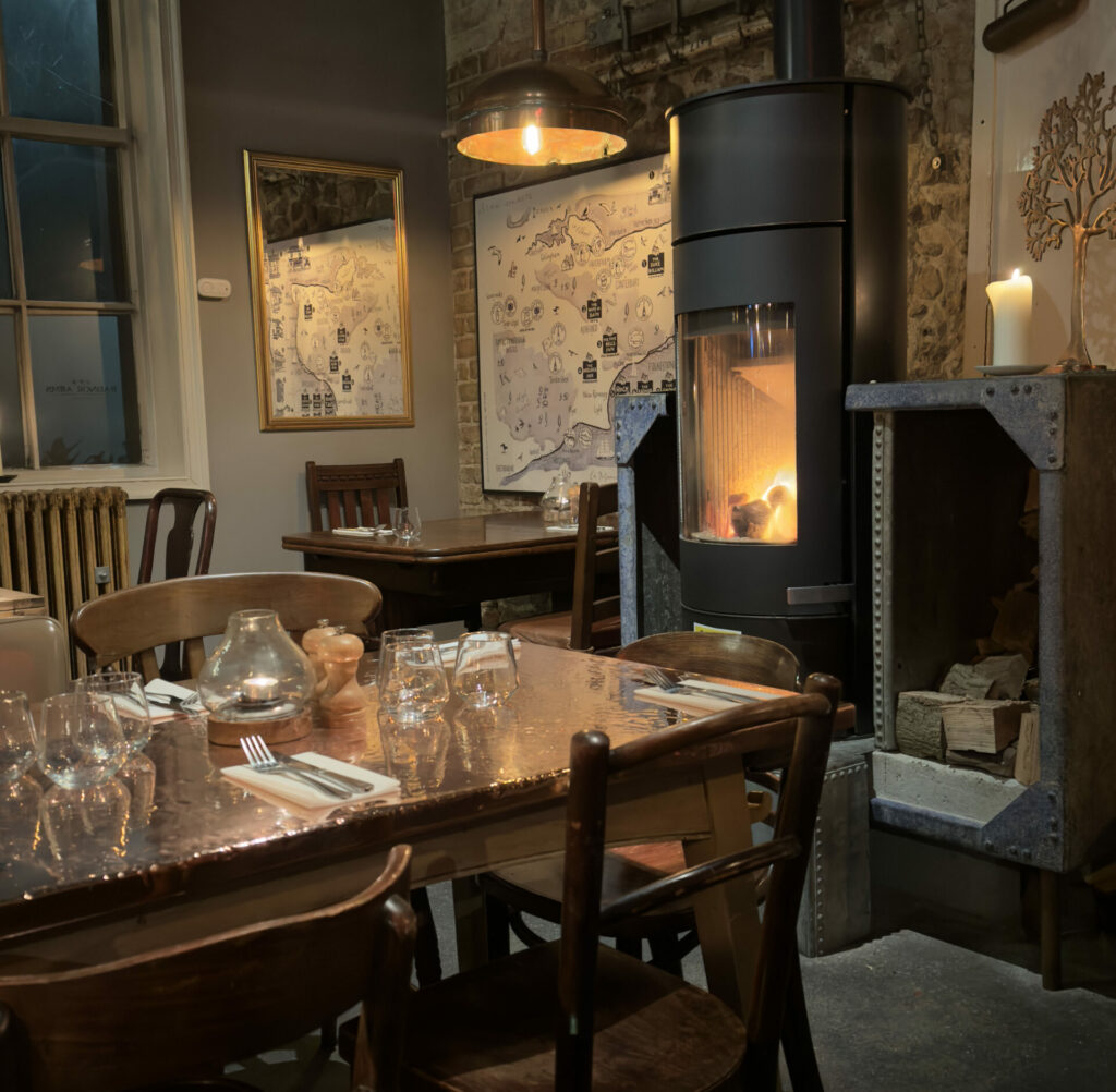 A view inside a pub showing a lit fireplace overlooking brown wooden tables