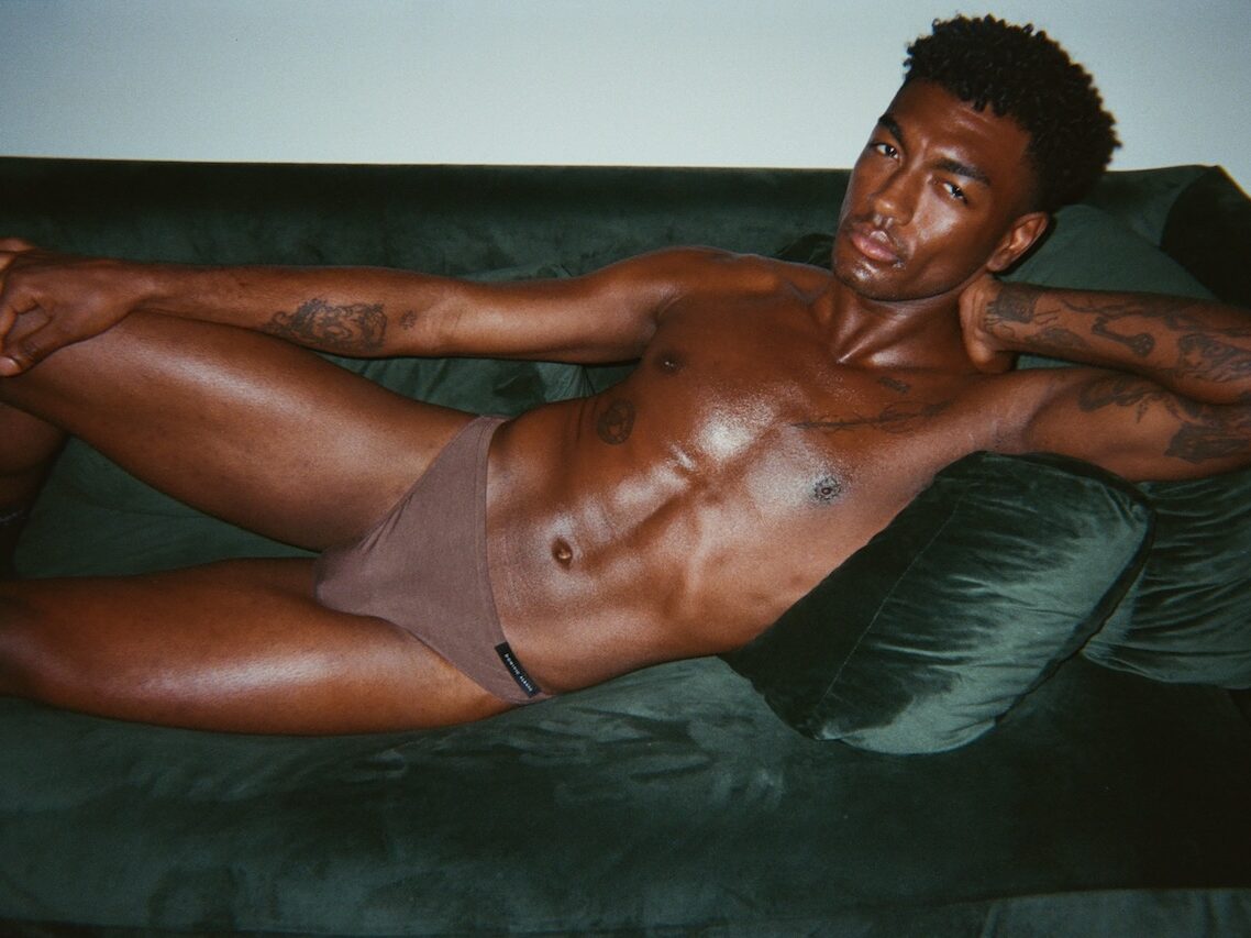 a man in brown underwear lying a green sofa