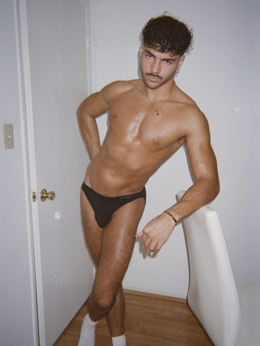 a man with a moustache standing in a pair of black briefs