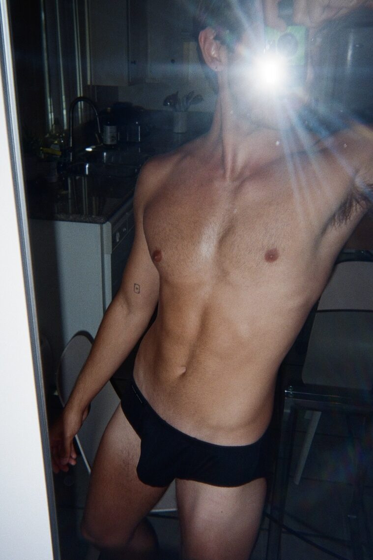 a man in black underwear with face hidden by a camera flash