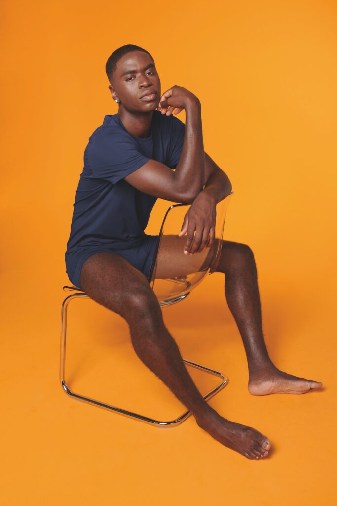 a man in black t-shirt and shorts sat down against an orange background