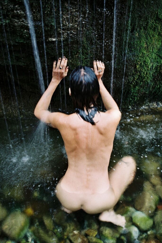 a naked person kneeling by a waterfall