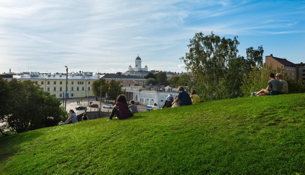 People sat on grass looking at the Helsinki skyline in the distance