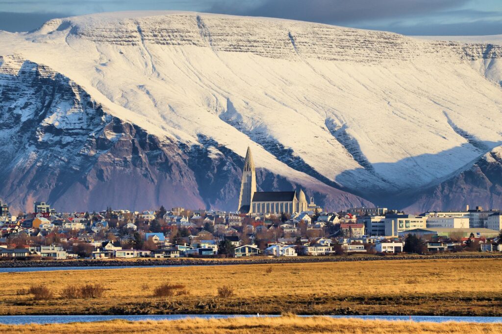 Cityscape of Reykjavik with a snow covered mountain behind it.