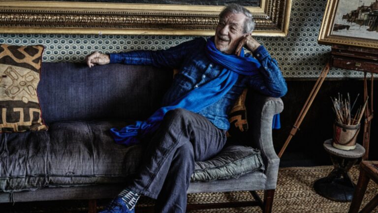 Sir Ian sitting on a sofa in a blue top and dark blue trousers